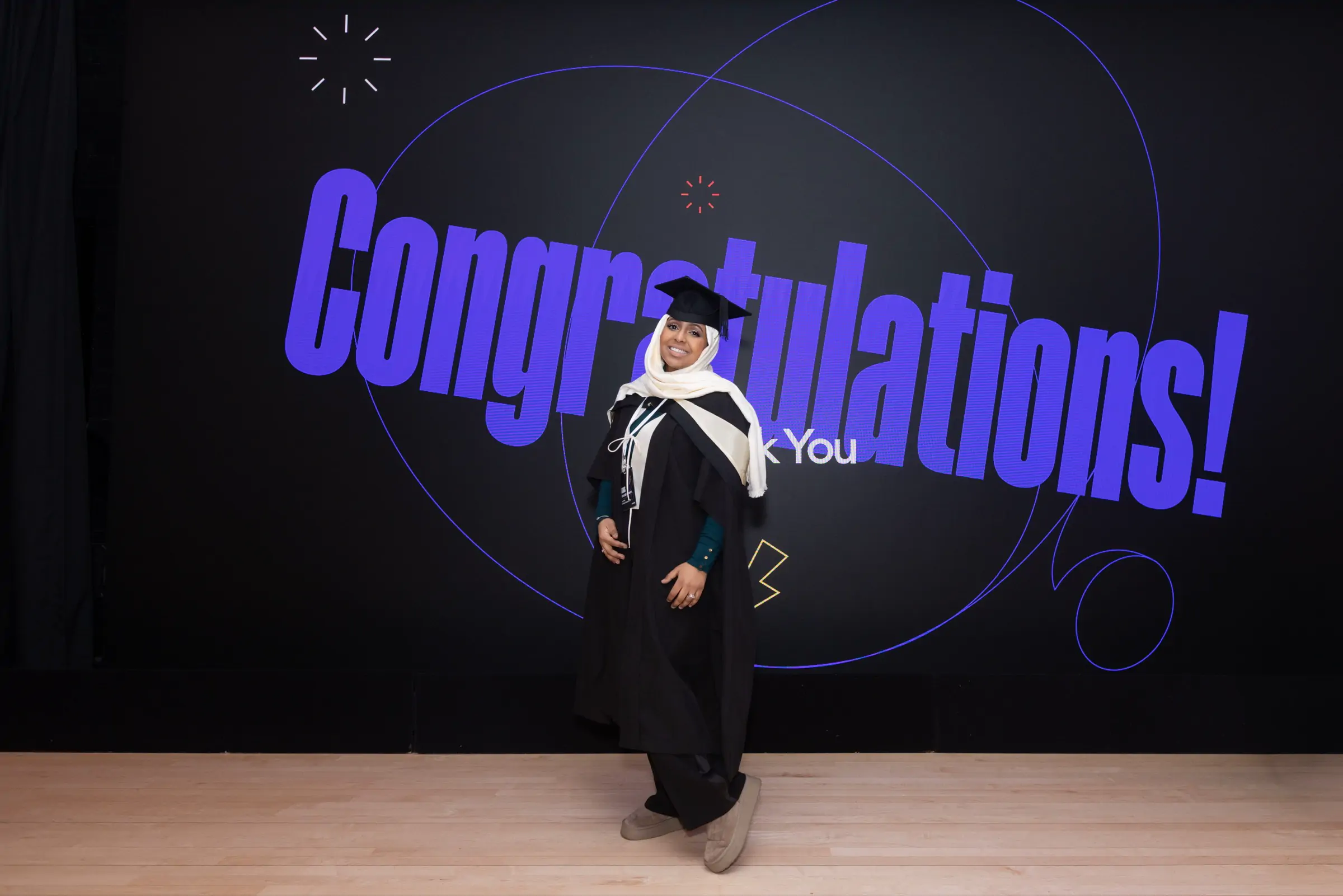Ines Abdalla standing alone on stage in front of a large Congratulations! screen