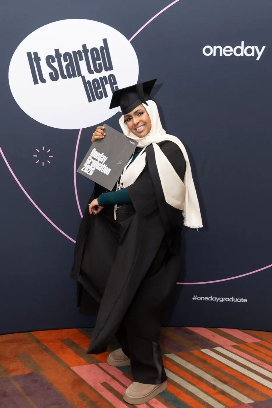 Full-length portrait of Ines Abdalla in cap and gown in front of the graduation backdrop